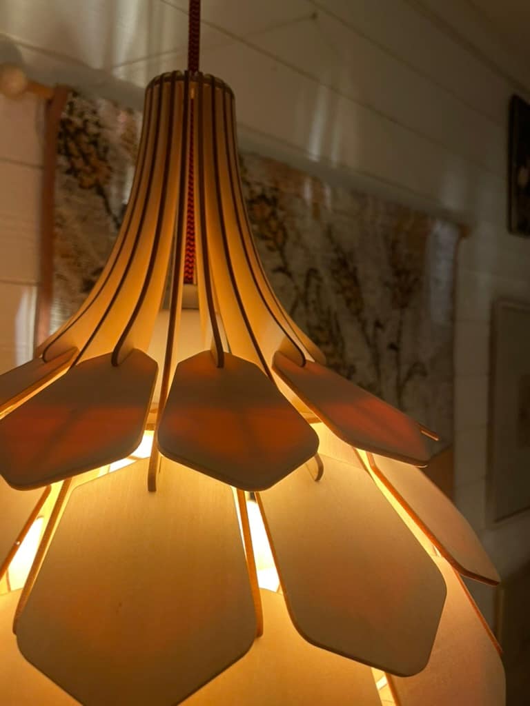 Närbild av en modern lampa med hexagonala skärmar som avger varmt ljus, hängande i en inredningsmiljö.